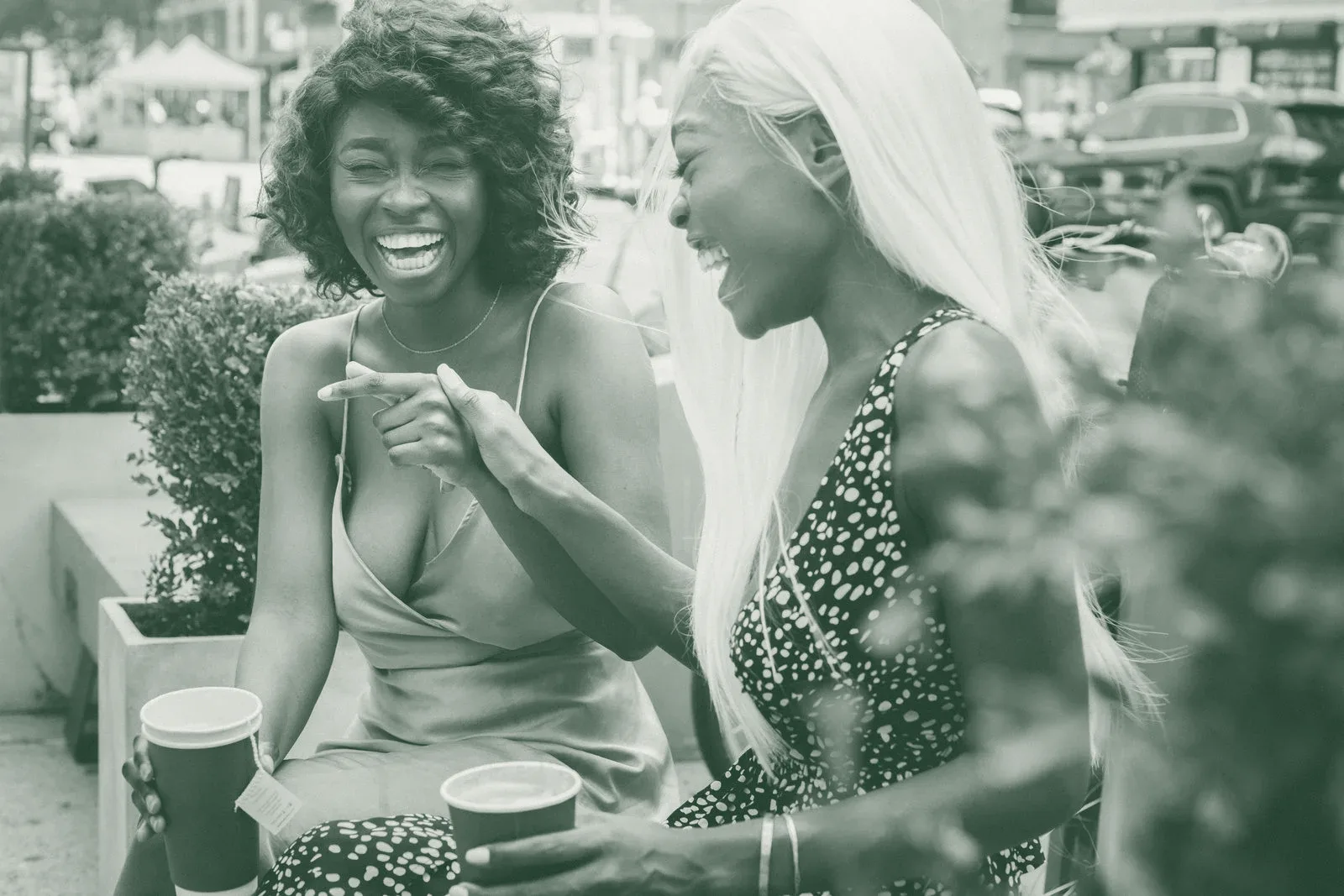 Two women laughing together over coffee outdoors
